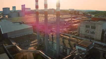 Wall Mural - Aerial view of industrial area with warehouses, factory buildings and chimney on foreground at sunset, drone footage