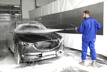 Canvas Print - Worker cleaning automobile with high pressure water jet at car wash