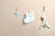 Knitted booties, pacifier and toy bunny hanging on washing line against color background. Baby accessories