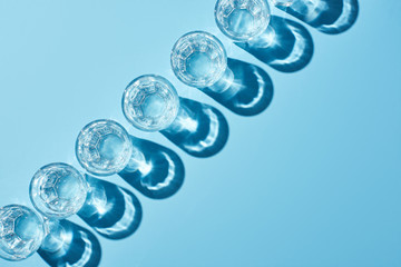 flat lay with glasses with clear water and shadows on blue background