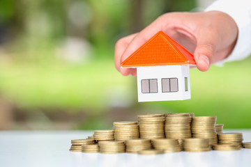 Human hand putting house model on coins stack,  planning savings money of coins to buy a home concept, mortgage and real estate investment.  saving or investment for a house.