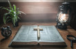 © surachat - Close up wooden christian cross putting on old holy Bible with light of oil lamp at worship room. christian concept.