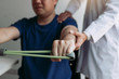 © wutzkoh - Asian male physical therapist descent working with patient doing stretching exercise with a flexible exercise band in clinic room.