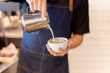 Barista hand pour milk making latte art coffee at cafe.