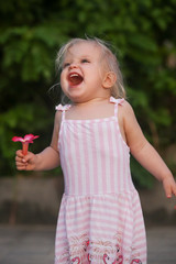 Cute girl in a pink dress holding a pink flower, candid outdoor portrait