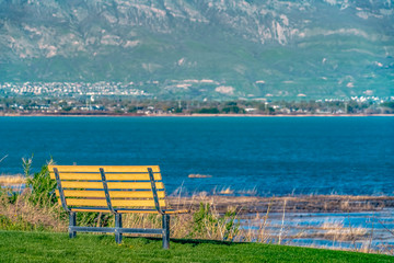 Close up of a bench facing a lake with glistening blue water on a sunny day