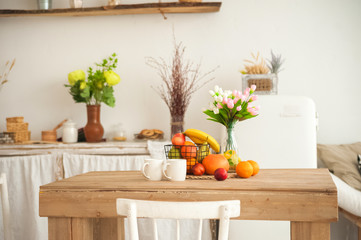 Wall Mural - Concept breakfast made from fruits and coffee or tea. Oranges, bananas, cups, peaches on a textural large wooden table against a background of rustic or Scandinavian cuisine