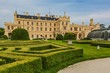 Lednice, Czech Republic - May 28 2019: Famous Lednice castle in South Moravia with yellow facade. Garden with green lawn, bushes and sand footpath. Sunny spring day, blue sky, white clouds.