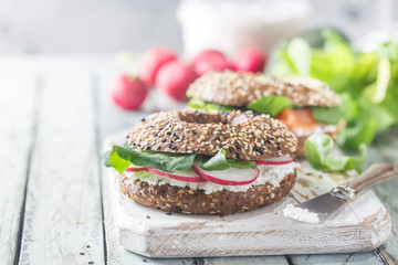 Bagels with cream cheese avocado, fish, arugula and radish on old wooden table. Healthy breakfast food.