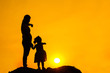 The family silhouette of the mother and child standing watch the sunset and the sky in orange in evening