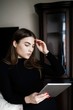© nazariykarkhut - Beautiful young woman in casual clothes is using a digital tablet and smiling while sitting on couch at home