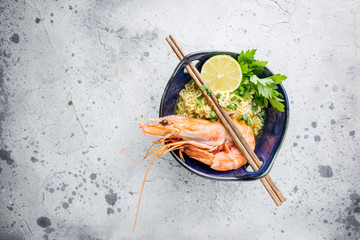 Wall Mural - A bowl of instant Chinese noodles with green onions, red hot chilli peppers, and shrimps on a gray stone background, top view