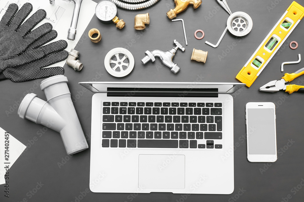 Modern laptop, mobile phone and plumber items on dark background