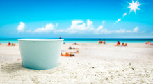 A Blue Metal Bucket With Free Space For Your Product. The Possibility Of Mounting Bottles With Drink, Ice Cream, Food Or Other Products. Blurry Beach With People And Ocean View.