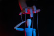 Concept of control. Marionette in human hand. Objects are colored on red and blue light.