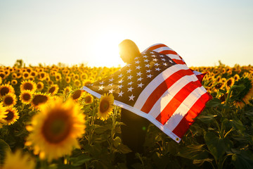 Beautiful girl with the American flag in a sunflower field. 4th of July. Fourth of July. Freedom. Sunset light The girl smiles. Beautiful sunset. Independence Day. Patriotic holiday. 