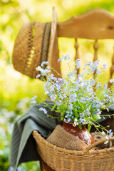 Vintage wooden chair standing in the garden with wicker basket, ceramic vase and bouquet of forget-me-not's on it. Close up