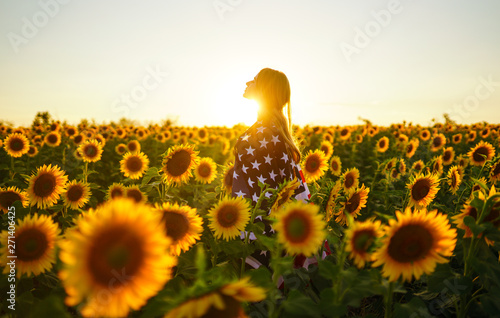 Foto  Beautiful girl with the American flag in a sunflower field