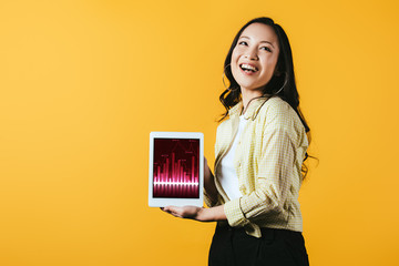 Wall Mural - smiling asian girl showing digital tablet with graph, isolated on yellow