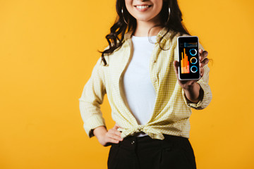 Wall Mural - cropped view of brunette girl showing smartphone with infographic, isolated on yellow