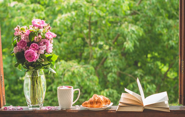 Book, croissant, cup of tea and roses on a wooden window. Read books. Romantic concept. Vintage style 