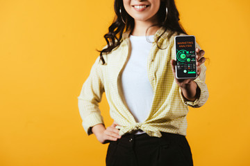 Wall Mural - cropped view of brunette girl showing smartphone with marketing analysis, isolated on yellow