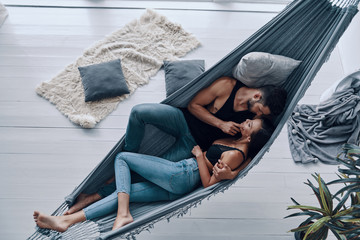 Wall Mural - Loving everything about her. Top view of beautiful young couple embracing and smiling while resting in the hammock indoors