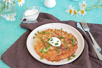 Wall Mural - Roshty, fried potato pancake from boiled potatoes on a white clay plate on a turquoise background. Served with sour cream. Swiss cuisine.