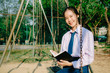 © TeTe Song - Lovely teenage girl wearing school uniform reading book while sitting on a swing at the park .