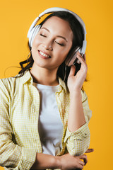 Wall Mural - smiling asian girl listening music with headphones, isolated on yellow