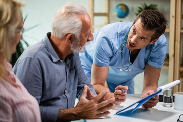 Wall Mural - Male doctor analyzing medical documents while talking with senior couple.