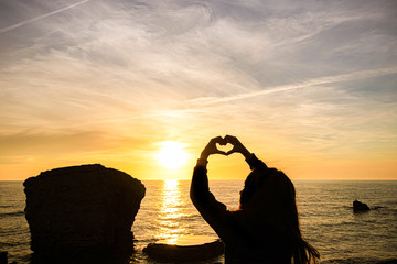 Wall Mural - girl silhouette on sunset sea background. the girl depicts a heart from her hands.