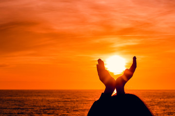 Wall Mural - girl silhouette on sunset sea background. girl holds the sun in his hands.