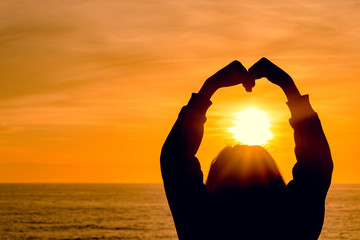 Wall Mural - girl silhouette on sunset sea background. the girl depicts a heart from her hands.