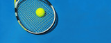 Summer sport concept with tennis ball and racket on blue hard tennis court. Flat lay, top view, copy space. Blue and yellow, banner size.