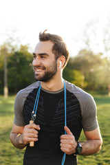 Handsome young strong sports man posing outdoors at the nature park location with skipping rope.