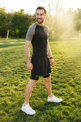 Handsome young strong sports man posing outdoors at the nature park location make exercises with fitness equipment.