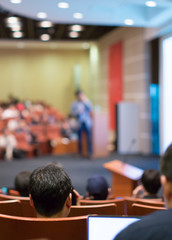 Blurred speaker giving speech at business seminar in auditorium. Background of presenter in hall meeting during public lecture. Defocused businessman in conference hall with bokeh.