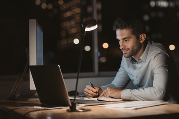 Young businessman writing down notes while working at night