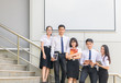 © kwanchaichaiudom - Students stand and smile on stairs with white billboard