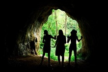 Female Silhouettes At The Entrance To Natural Cave In The Forrest.