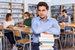 © JackF - Tired man sitting with pile of books in university library on background with working fellow students