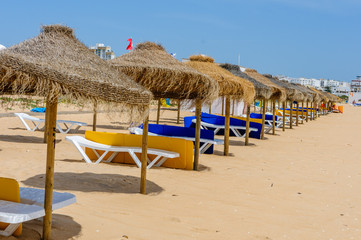 Rows of straw parasols and sunloungers on the beach at Vilamoura, Algarve, Portugal.