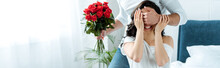 partial view of man with bouquet of red roses closing woman eyes to make surprise in bedroom