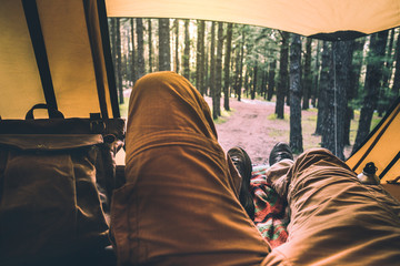 Wall Mural - Alternative point of view for people relaxing inside a tent with amazing view outside - forest with trees and wood on background - altrnative vacation travel man with backpack enjoying the nature