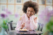 © chika_milan - Portrait of charming positive mixed race woman in pink turtleneck sweater sitting in confectionery and eating gateau.