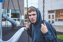 Sad Teenager Sitting On A Swing Outside Of A School. He Is Reminiscing About When He Was Younger.