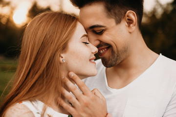 Wall Mural - Side view portrait of a lovely couple dating outside face to face with closed eyes smiling before kissing while is touching face of his girlfriend.