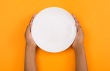 Female Hands Holding Empty Plate On Orange Background