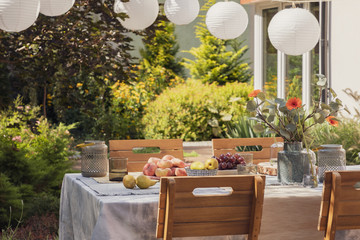 Wall Mural - Garden with stylish wooden furniture and table with fruits and flowers, real photo